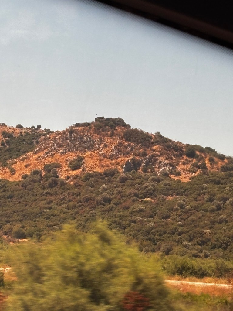 A landscape view of rolling hills in Turkey, showcasing dry grass and greenery under a clear blue sky.